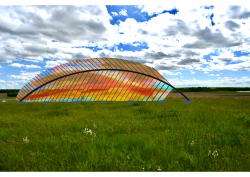 Artist rendering of a huge colorful grey feather arching over green prairie grasslands with a partly cloudy sky above