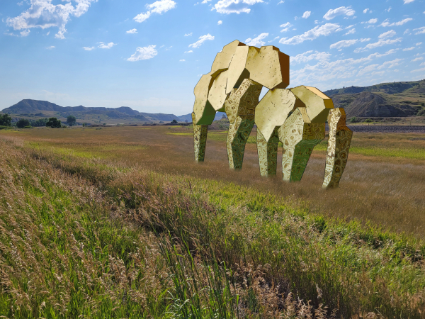 prairie grasslands with North Dakota badlands in the background and a baby blue sky above, featuring a modern sculpture in the middle that looks somewhat like a horse and bison